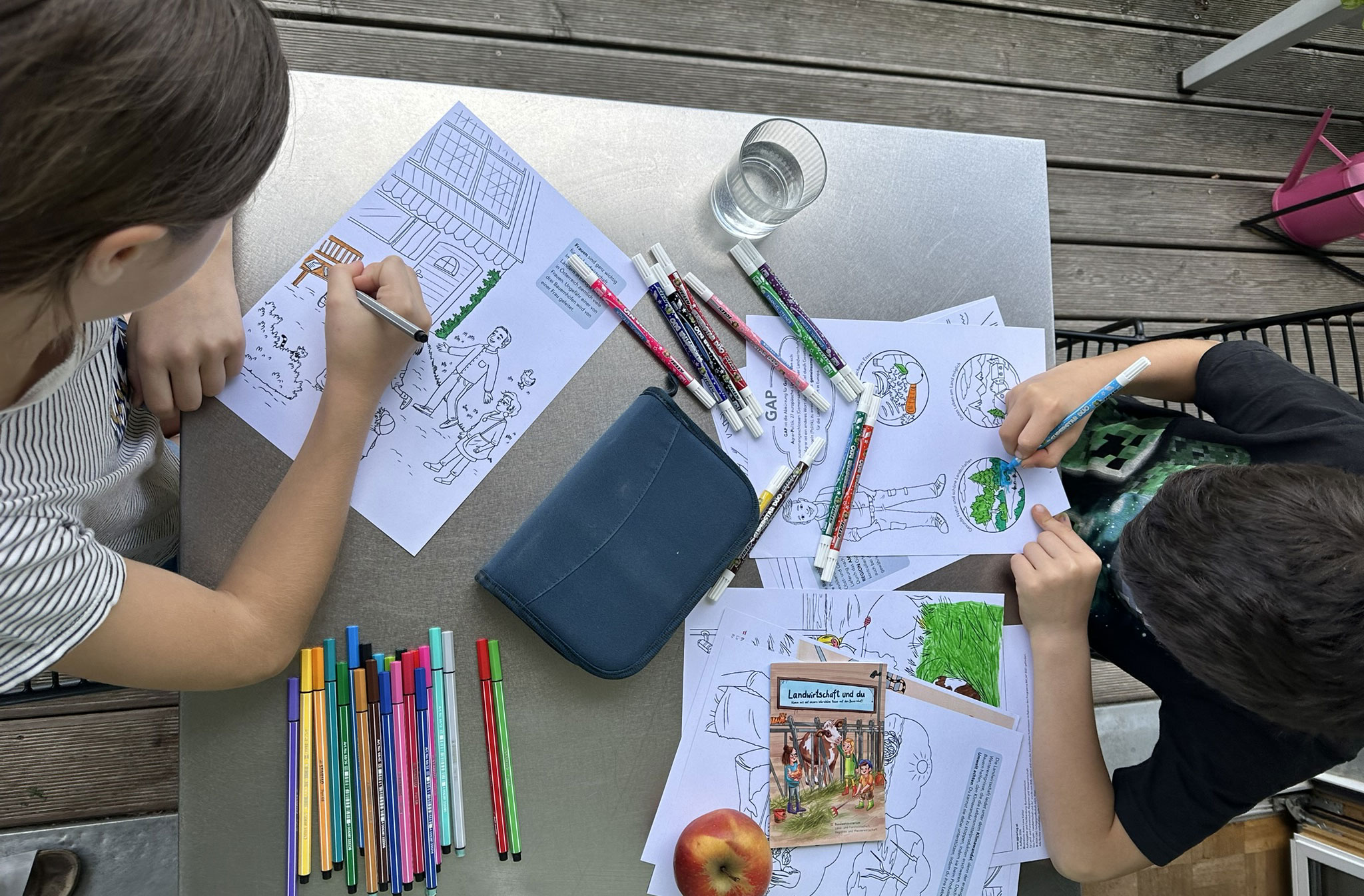 Kinder sitzen am Tisch und malen Malbuch aus.